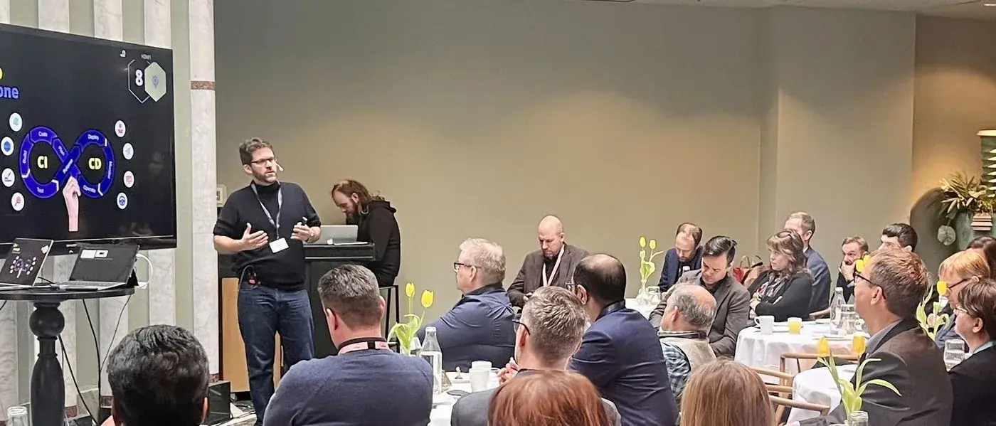 Mario A. Brückner speaking to a full conference hall seated at round tables